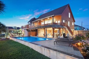 A two-story house with a swimming pool, outdoor seating, and a covered patio area.