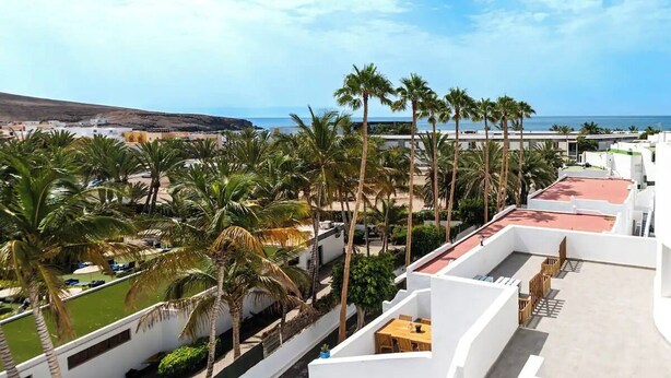 Un hôtel en bord de mer doté d’une terrasse sur le toit, de palmiers et offrant une vue sur la mer.