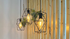 Une table à manger agrémentée de luminaires suspendus aux formes géométriques, une bouteille de vin et une machine à café.