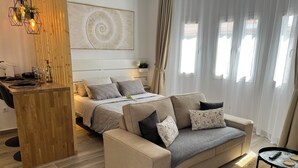 Une chambre moderne avec un lit, un canapé, un bureau en bois et une grande fenêtre avec des rideaux.