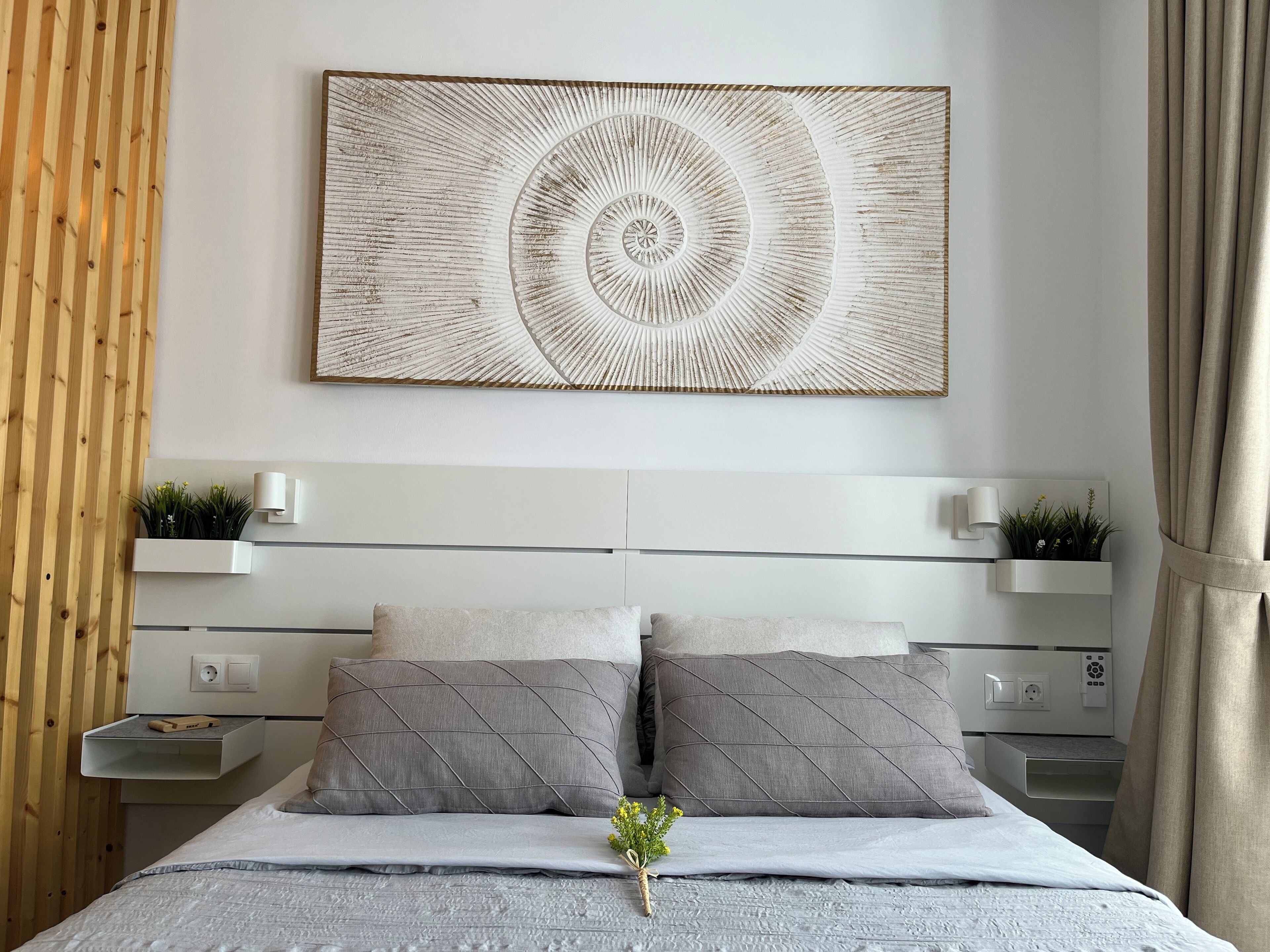 A modern bedroom with a central bed, two bedside tables, and a wall-mounted artwork.