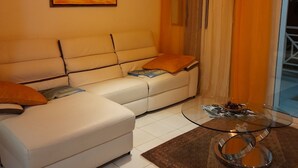 Una sala de estar con un sofá blanco, una mesa de centro de vidrio y un cuadro en la pared.