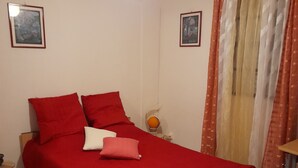 Un dormitorio con cama, ropa de cama roja, una mesita de noche, una l ámpara y dos cuadros en la pared.