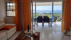 Una sala de estar con un sofá, una mesa de centro de vidrio y vistas al mar a través de amplios ventanales.