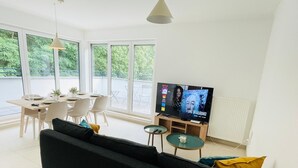 Ein modernes Wohnzimmer mit Sofa, Esstisch, Stühlen und Fernseher.