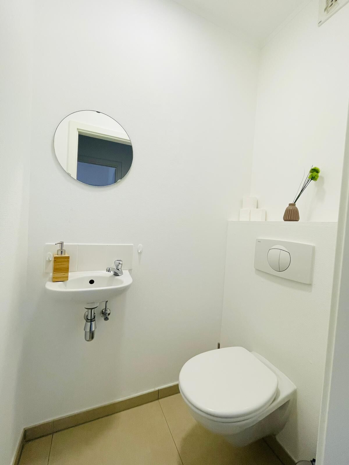 Un baño pequeño y limpio con lavamanos, espejo, inodoro y un interruptor de luz en la pared.