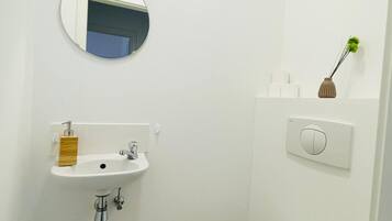 Un baño pequeño y limpio con lavamanos, espejo, inodoro y un interruptor de luz en la pared.