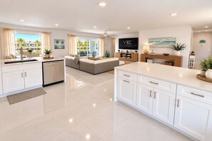 Una cocina moderna con armarios blancos, una isla central y un área de comedor con sofá y mesa.