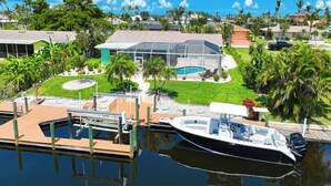 A house with a pool, surrounded by lush greenery and a dock with a boat. - VRCC Villa Blue Pelican - Waterfront style & comfort (Cape Coral)