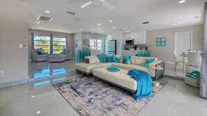 A spacious living room with a large sectional sofa, a ceiling fan, and a kitchen area in the background. - VRCC Villa Blue Pelican - Waterfront style & comfort (Cape Coral)