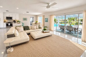 A modern living room with a sectional sofa, a small round table, and a view of a pool through large glass doors.