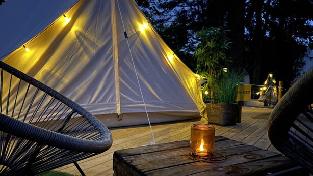 A tent with string lights, a candle on a wooden table, and chairs.