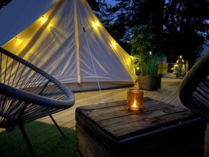Una carpa con luces de cuerda, una vela sobre una mesa de madera y sillas.