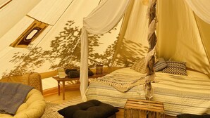 A cozy tent with a bed, a chair, a small table, and a window.