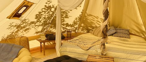 A cozy tent with a bed, a chair, a small table, and a window.