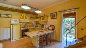 Une cuisine avec des meubles de couleur jaune, un plan de travail blanc, une cuisinière et un réfrigérateur. Il y a une fenêtre donnant sur des arbres et un escalier en bois.