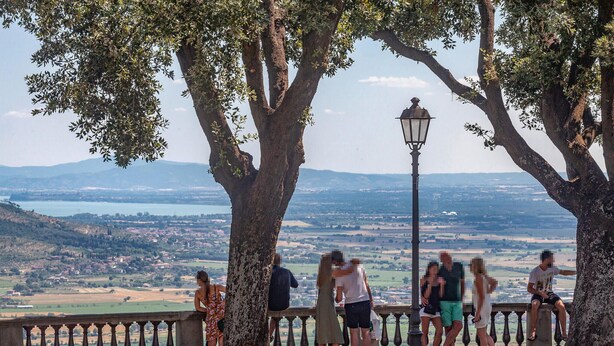 Un belvédère offrant une vue panoramique, agrémenté d’une balustrade en pierre, d’un lampadaire, et donnant sur une vallée avec un plan d’eau et des collines lointaines.