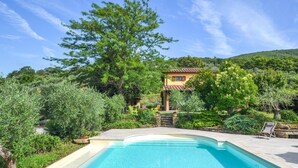 Une piscine entourée d’une végétation luxuriante et une villa avec un toit en tuiles.
