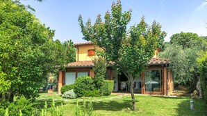 Une maison avec un toit en tuiles, un petit jardin et un arbre devant.