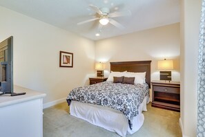 Une chambre à coucher comprenant un lit, des lampes de chevet, un ventilateur de plafond et un bureau avec un ordinateur et une télécommande.