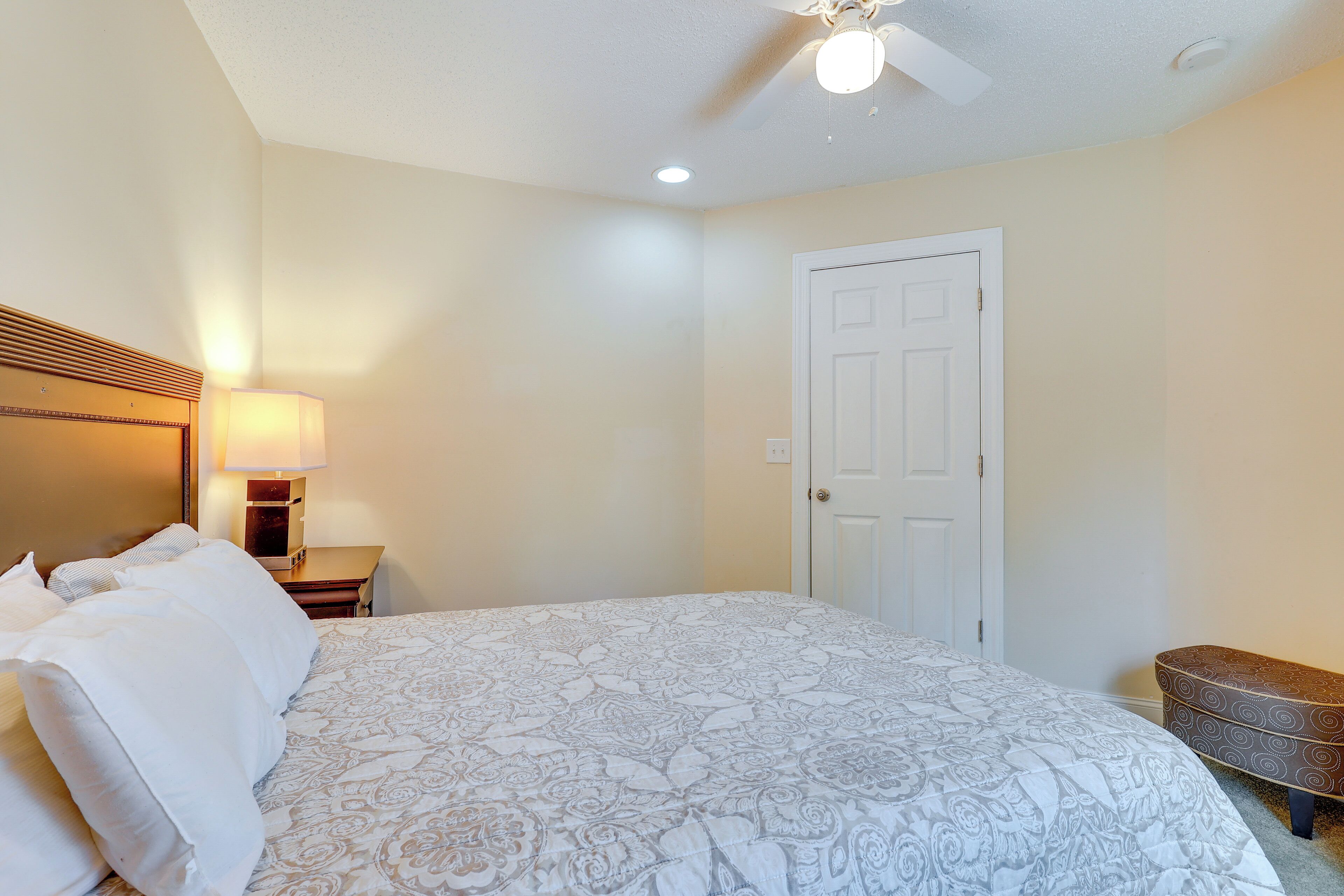 A bedroom with a bed, a nightstand, a lamp, a door, and a bench.