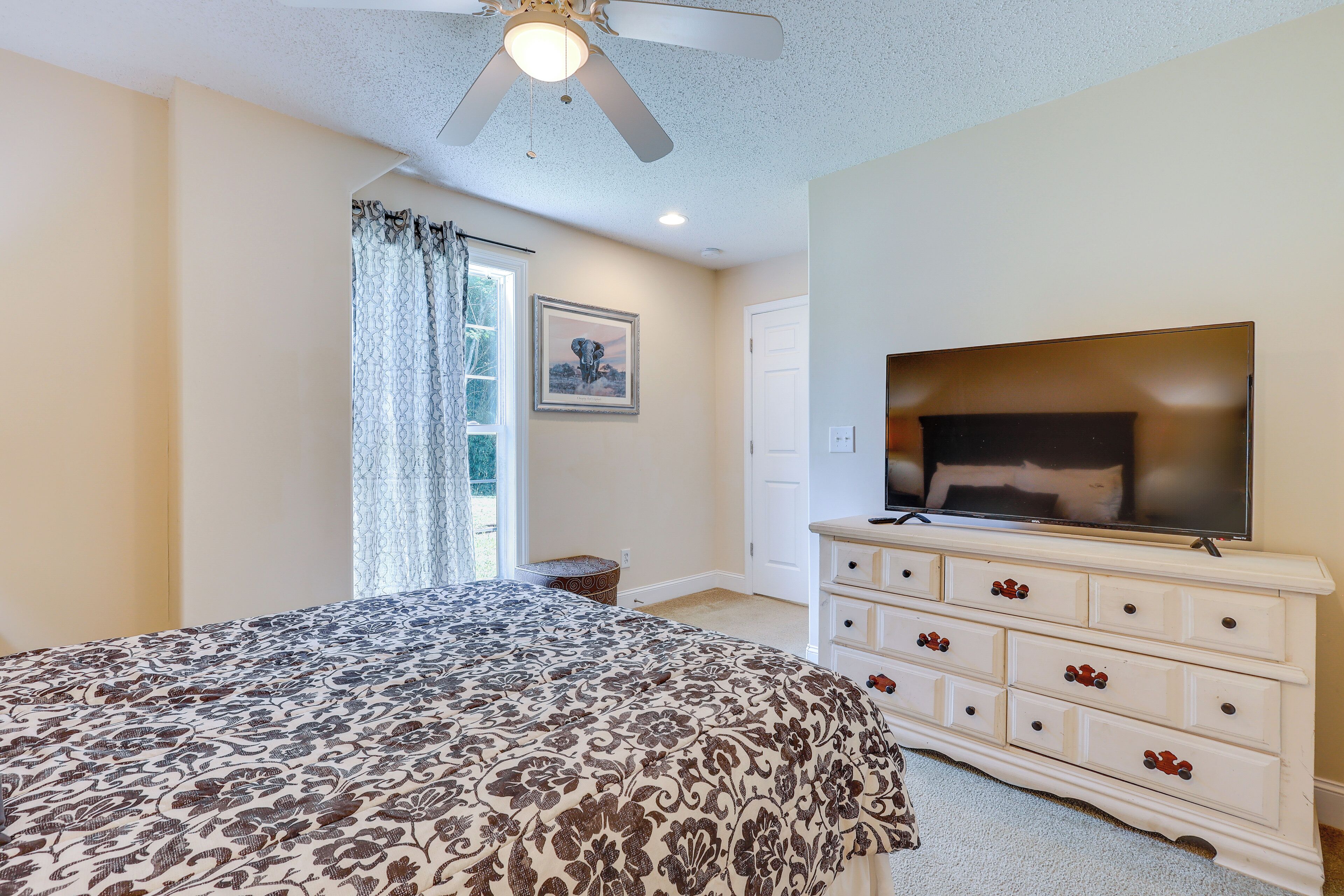A bedroom with a bed, dresser, television, and a ceiling fan.