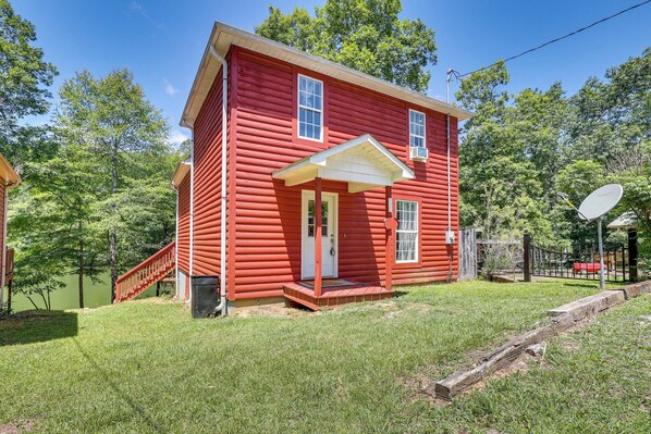 Une petite cabane en bois rouge avec une porte d’entrée blanche, un petit porche et une antenne parabolique.