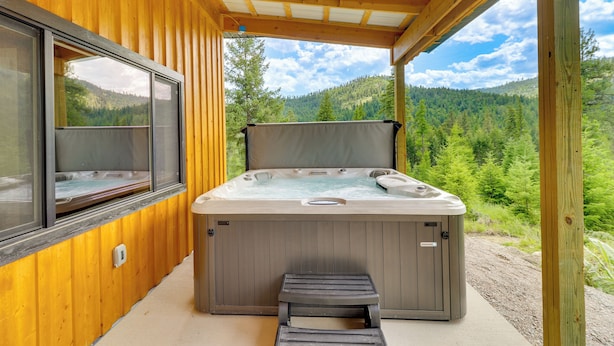 Een hottub in een houten blokhut met uitzicht op een bebost gebergte.