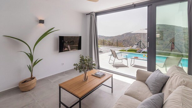 Una sala de estar moderna con un amplio ventanal que da a una piscina y montañas.