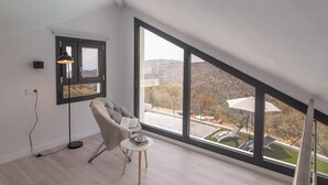 Una habitación moderna con un ventanal grande, un sillón cómodo, una mesita con un libro y una taza, y una lámpara de pie.