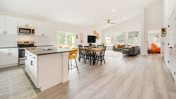 A spacious kitchen with white cabinetry, a central island, and a dining area with a round table and chairs. - Canyon Lake Oasis: Backyard & Wraparound Deck! (Canyon Lake)