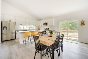 Een moderne keuken met witte kasten, roestvrijstalen apparatuur en een houten eettafel met zwarte stoelen.