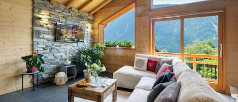 Un cuarto acogedor con pared de piedra, vigas de madera, un sofá, una mesa de centro y vista a las montañas.