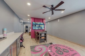 Une pièce avec un coin cuisine, un ventilateur de plafond, un mur rose et un tapis orné de motifs textuels.