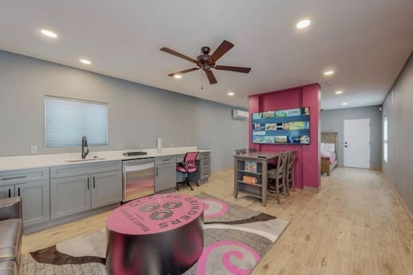 Une cuisine moderne avec des meubles de couleur grise, un mur d’accent rose et un ventilateur de plafond.