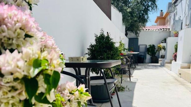 A patio area with round tables and chairs, surrounded by white walls and potted plants. - Larnaca - Studio - Sleeps 4 - Garden - Parking (Larnaca)