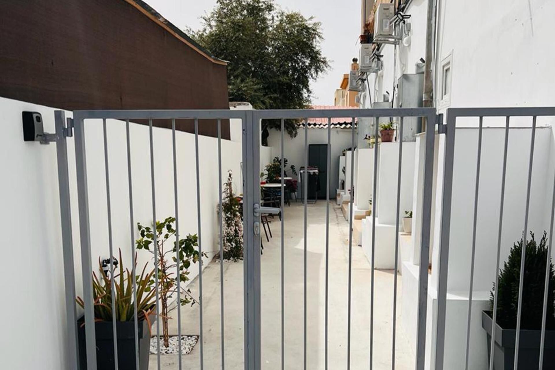 A gated courtyard with a table and chairs, potted plants, and a building with a tiled roof.