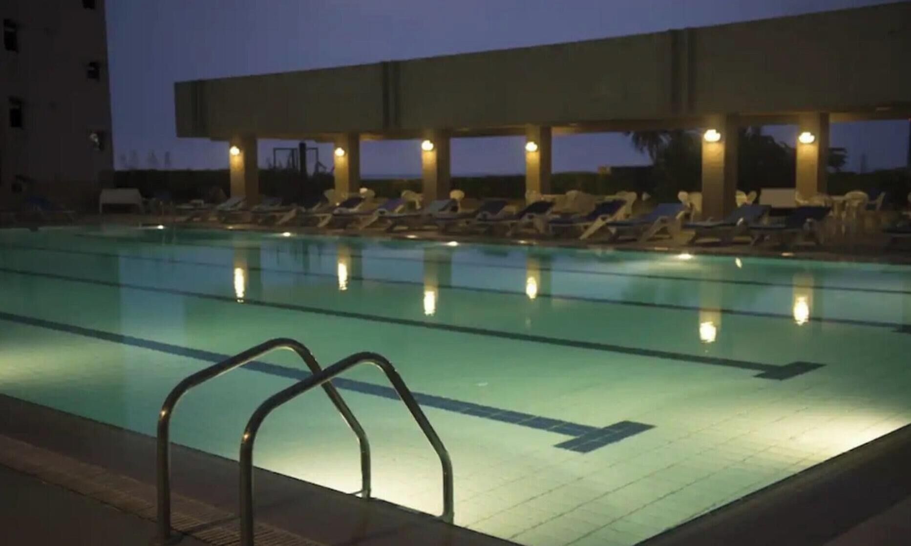 A swimming pool with lounge chairs and a covered area with lights.