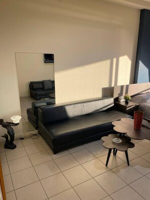 A modern living room with a dark sofa, a small round table, and a decorative sculpture. - Cozy Studio Retreat in Zouk Mosbeh (Zouk Mosbeh)