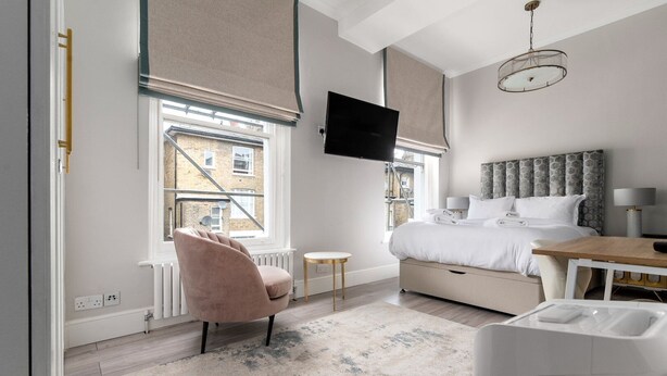 A modern bedroom with a bed, a TV, a chair, and a small table. - GuestReady - Modern Studio | Kensington Gem (London)
