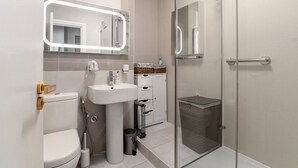 A modern bathroom with a toilet, sink, and glass-enclosed shower. - GuestReady - Modern Studio | Kensington Gem (London)