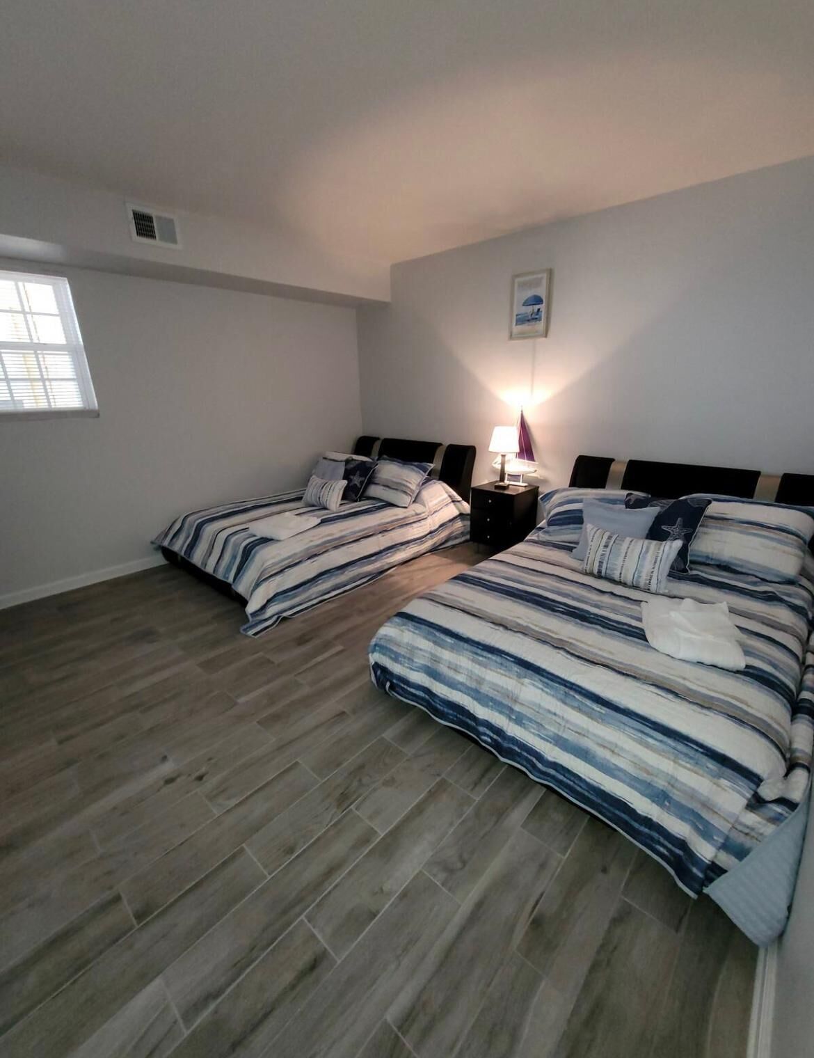 Een slaapkamer met twee bedden, een nachtkastje, een lamp, een raam en een aan de muur bevestigd schilderij.