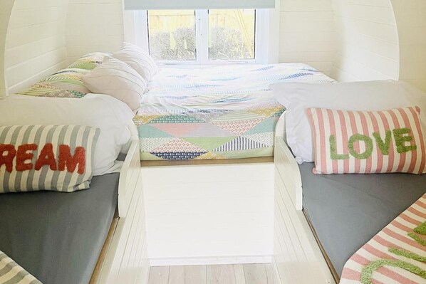 A cozy room with a bed centered between two gray sofas, adorned with colorful pillows and a patterned quilt. - Solo Glamping Pod - Sleeps 4 - Northumberland (Morpeth)