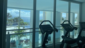A gym with exercise bikes and a view of a pool and palm trees.