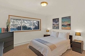 A bedroom with a large bed, two bedside tables, a window with a view, and two wall-mounted paintings. - South Douglas Gem With Mountain and Ocean View Hosted By William & Melissa (Juneau)