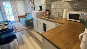 Une cuisine de taille réduite avec des meubles blancs, un plan de travail en bois, un évier et un four à micro-ondes.