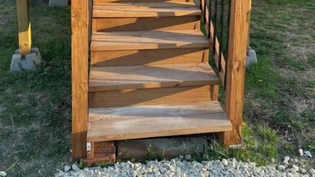 Un escalier en bois mène à un bâtiment doté d’une porte et de fenêtres en verre.