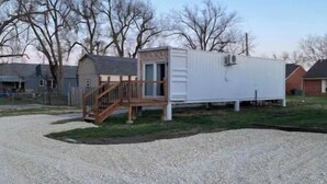 Une petite maison mobile d’un seul étage, dotée d’une terrasse en bois et d’un escalier menant à une porte.