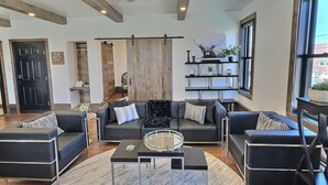 Ein modernes Wohnzimmer mit einem schwarzen Ledersofa, einem Glastisch und einer Holzbalkendecke.