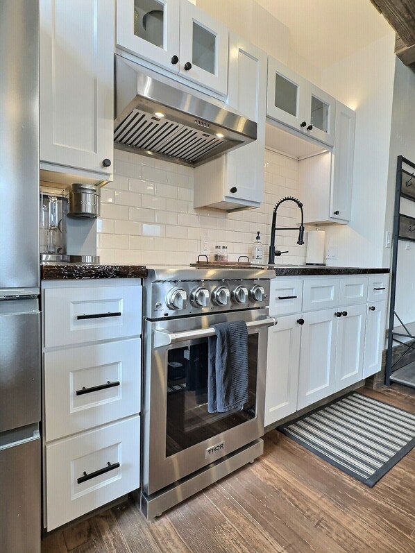 A modern kitchen with white cabinets, stainless steel appliances, and a wooden floor.